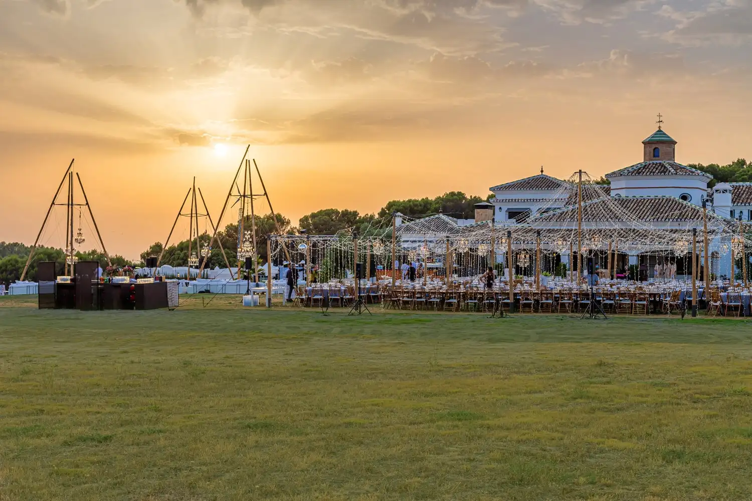 El sol bajo sobre el prado, con estructuras de madera y la mesa del banquete montada junto a la casa
