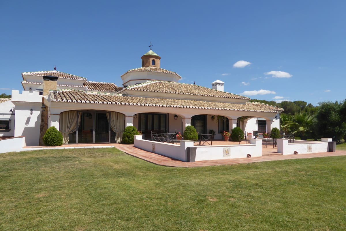La casa principal de Cortijo Curiel vista desde el césped: el porche de arcos, la cúpula sobre el tejado de teja y los olivos al fondo